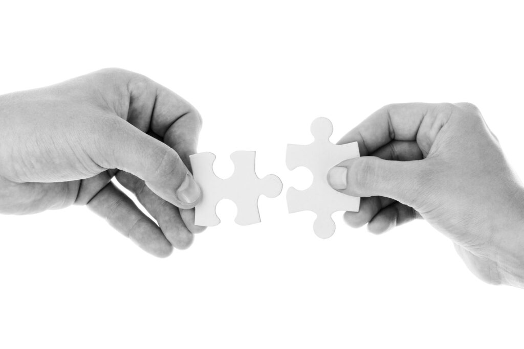 Two hands fitting together two white puzzle pieces on a clean white background, symbolising collaboration and problem-solving.
