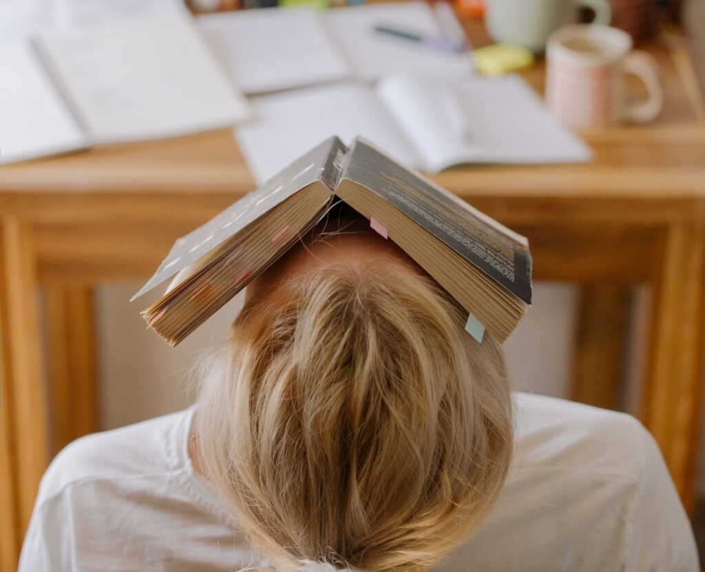 A student taking a rest from learning at a computer desk using positive study motivation tips. He has the book over his face.