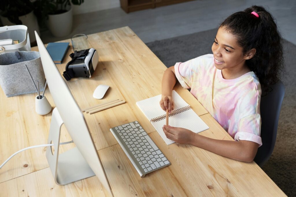 A smiling student at a wooden desk using an online 11Plus Guide on a computer screen for grammar school prep